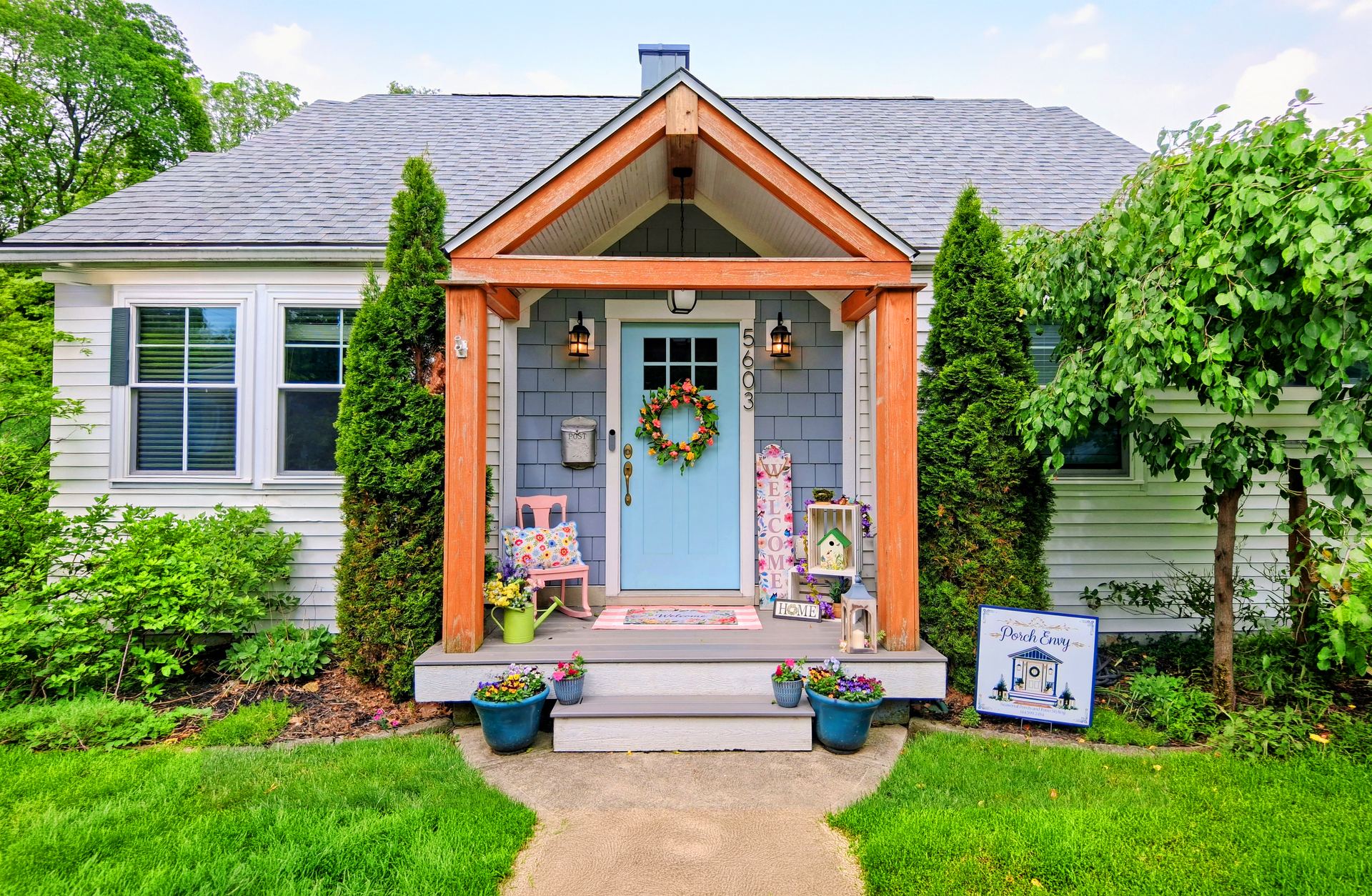 The same porch styled by Porch Envy — wreath on the door, rocking chair, seasonal flowers and welcome signs